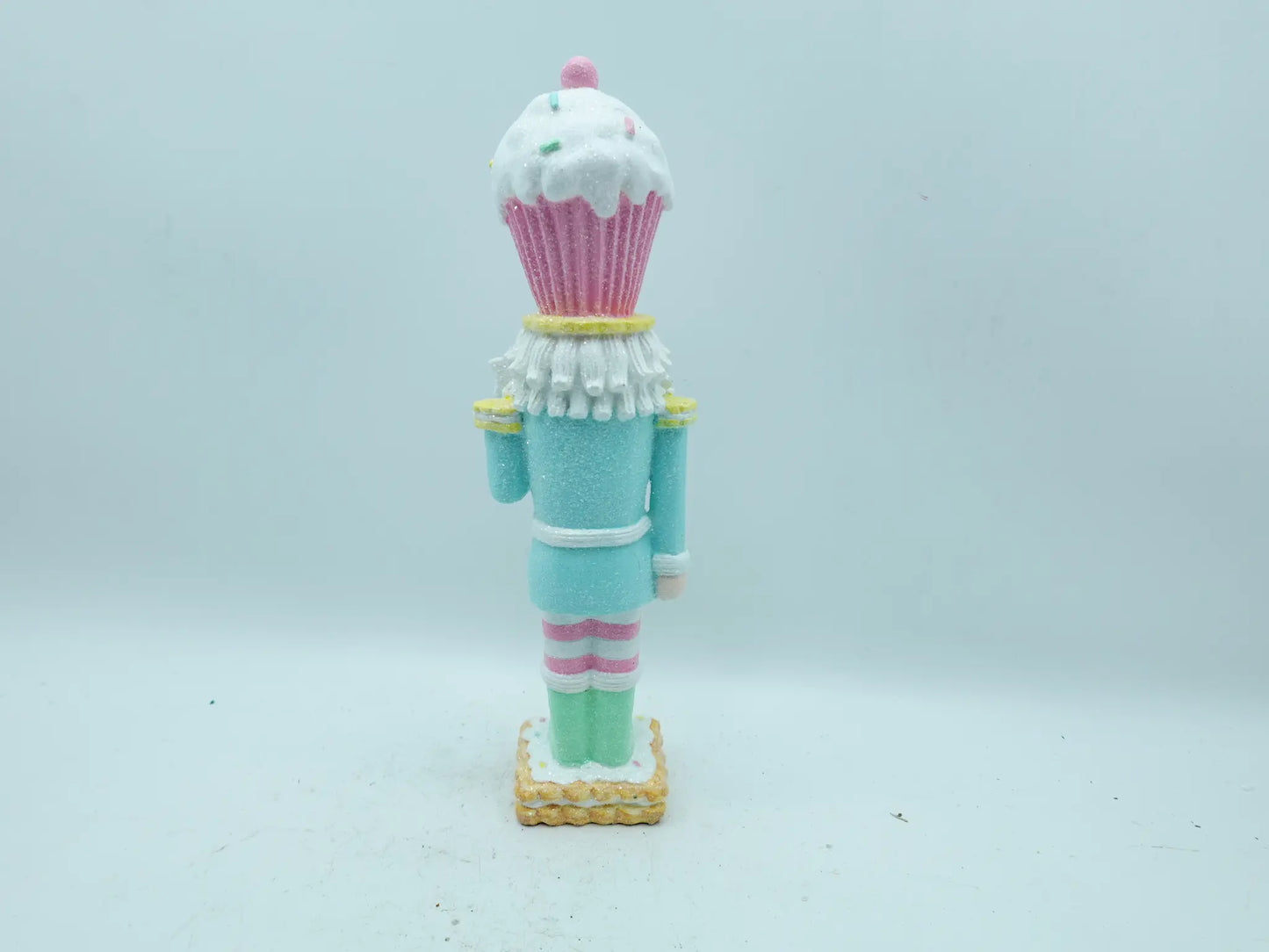 A cupcake-themed nutcracker figurine shown from the back, standing on a small gold base against a plain light gray background.