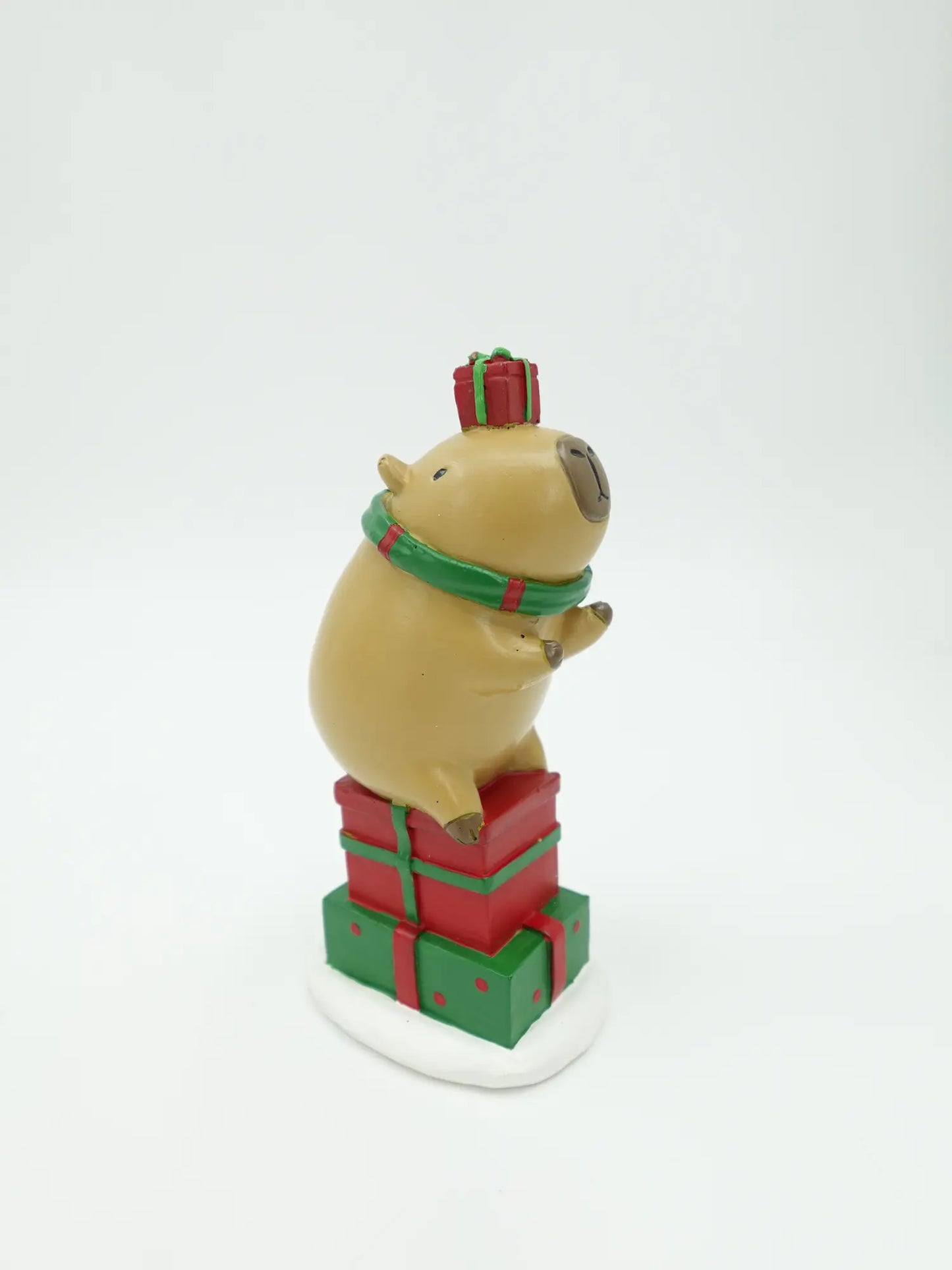 the hand-painted capybara figurine on stacked red and green gift boxes with a tiny red present on its head