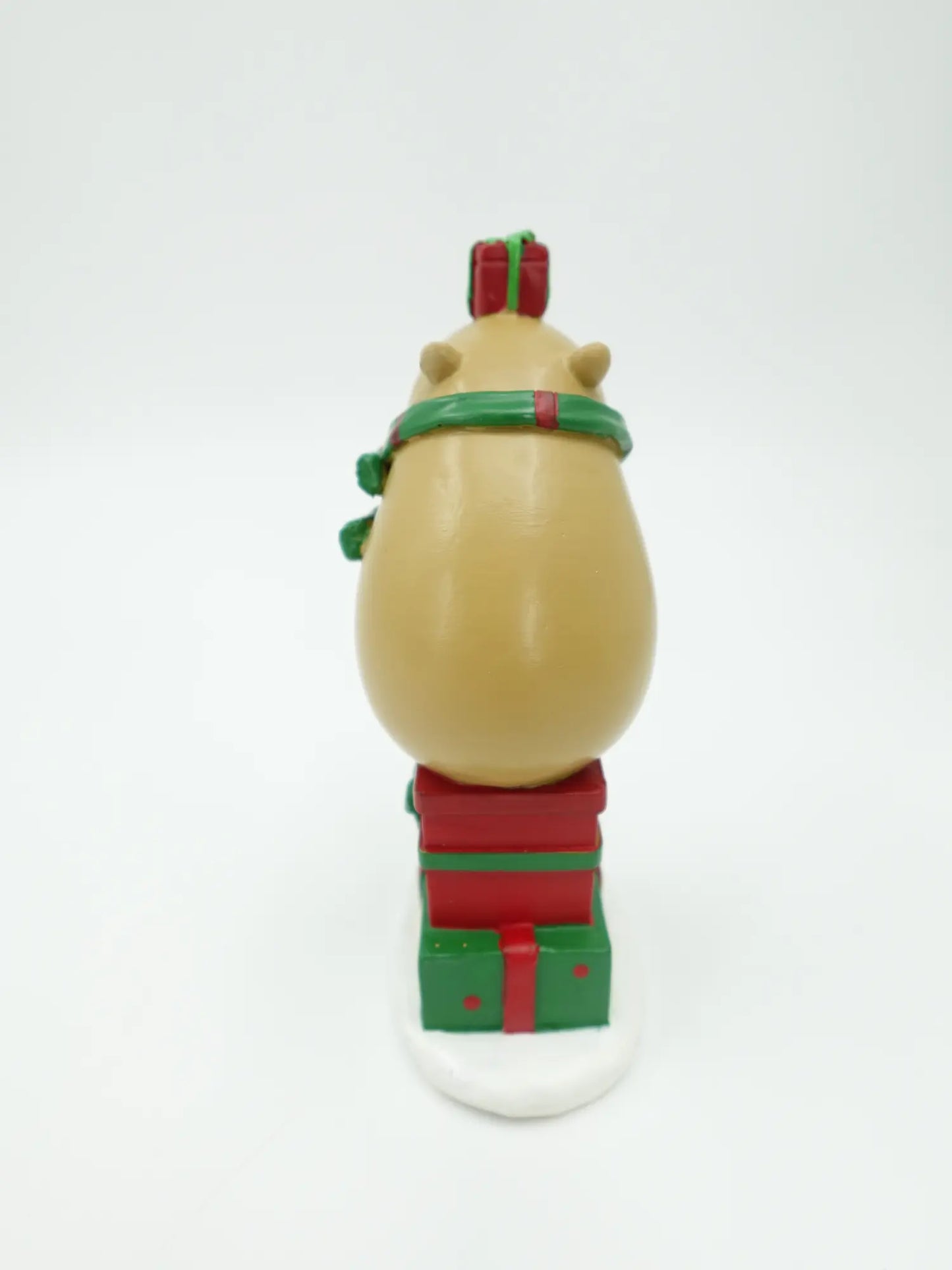 the capybara gift stack figurine showing the green scarf ends, rounded back, and gift box tower from behind