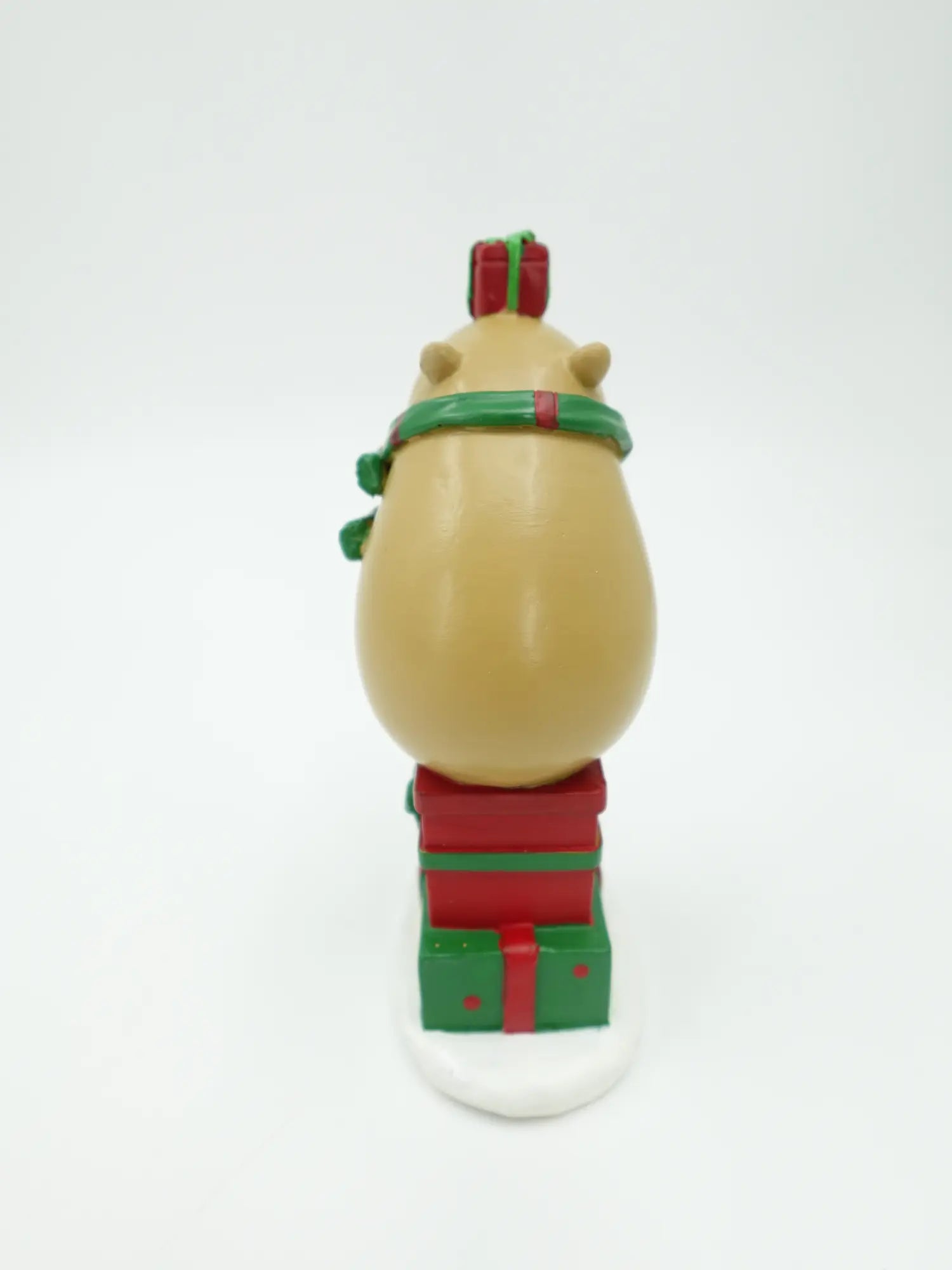 the capybara gift stack figurine showing the green scarf ends, rounded back, and gift box tower from behind