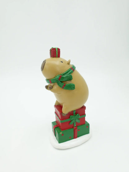 A holiday capybara figurine, showing the green scarf drape, stacked box profile, and snowy base detail.