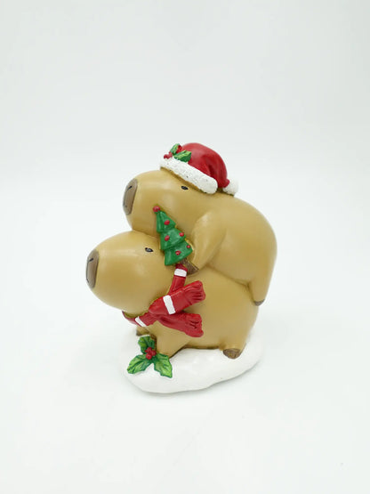 A holiday figurine of two stacked capybara on a white base, decorated with a red Santa hat, a green Christmas tree