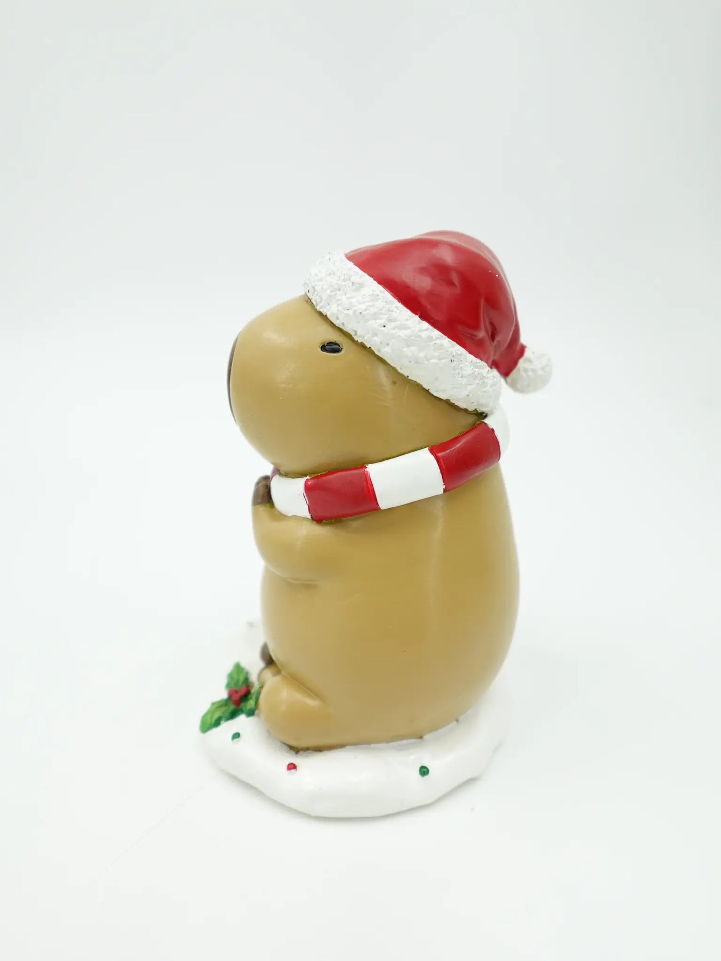 A resin capybara figurine wearing a red and white Santa hat and a red and white striped scarf, sitting on a white base
