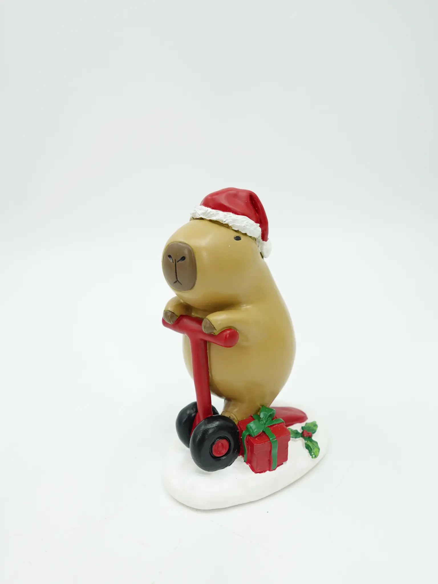 the hand-painted capybara figurine on red scooter with black wheels and red gift box with green ribbon