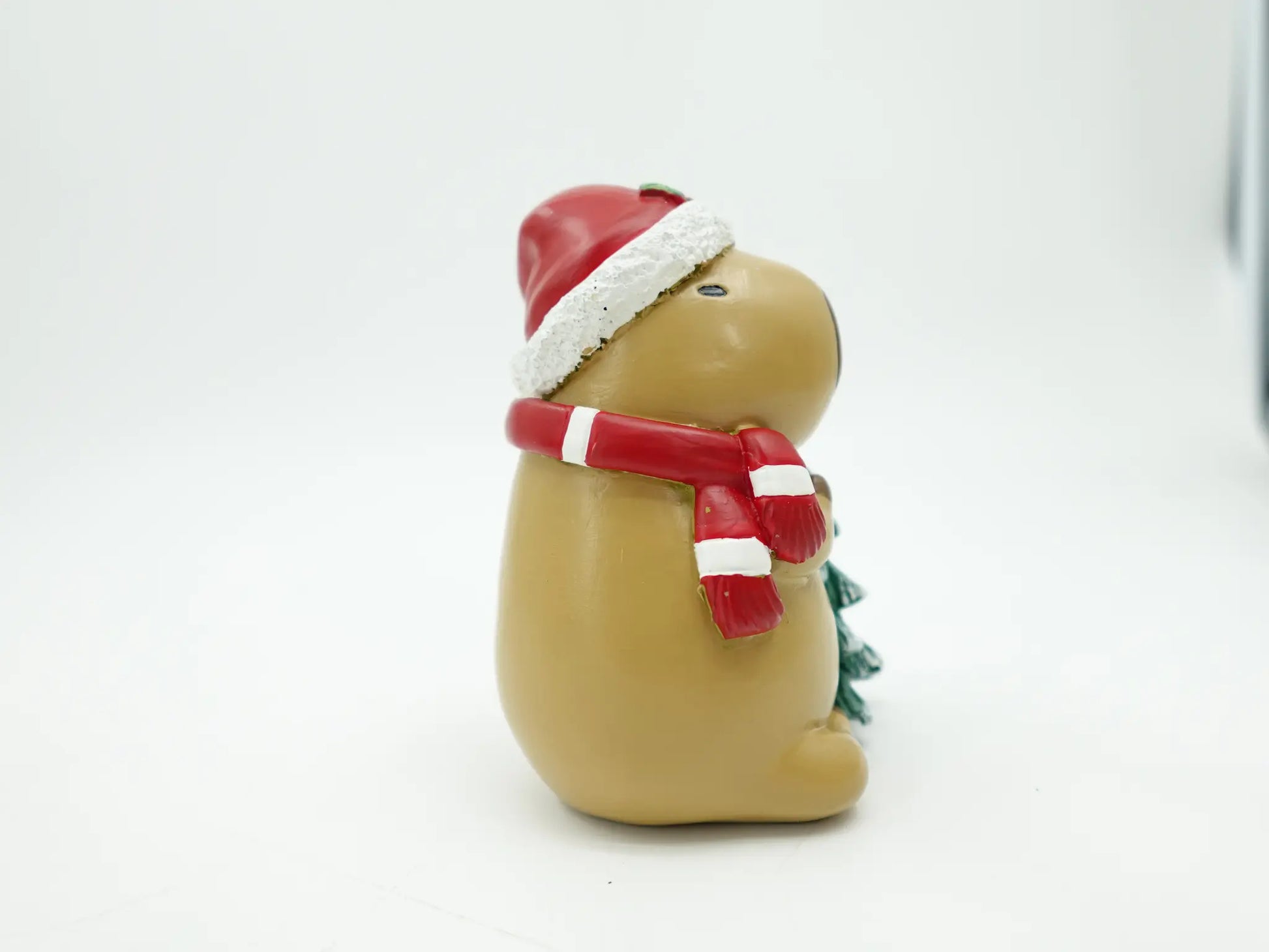 the resin capybara figurine showing the Santa hat pom-pom and candy-cane striped scarf, side view