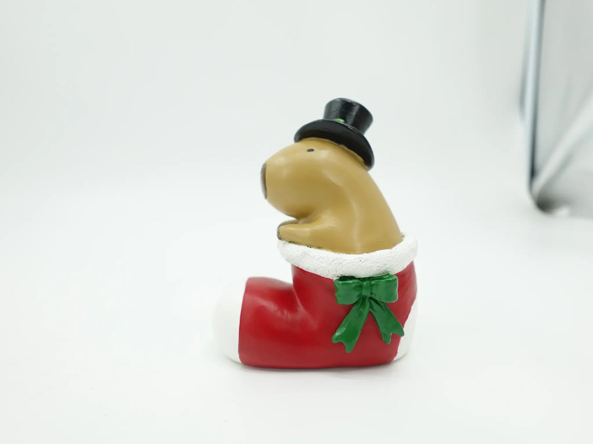 A holiday figurine of a capybara sitting inside a red Christmas stocking, photographed on a plain light background.