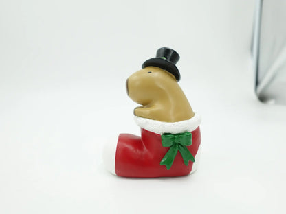 A holiday figurine of a capybara sitting inside a red Christmas stocking, photographed on a plain light background.
