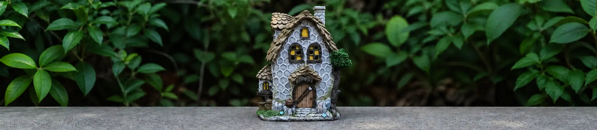 A fairy house figurine with a gray stone-textured body, brown roof, and glowing yellow windows.