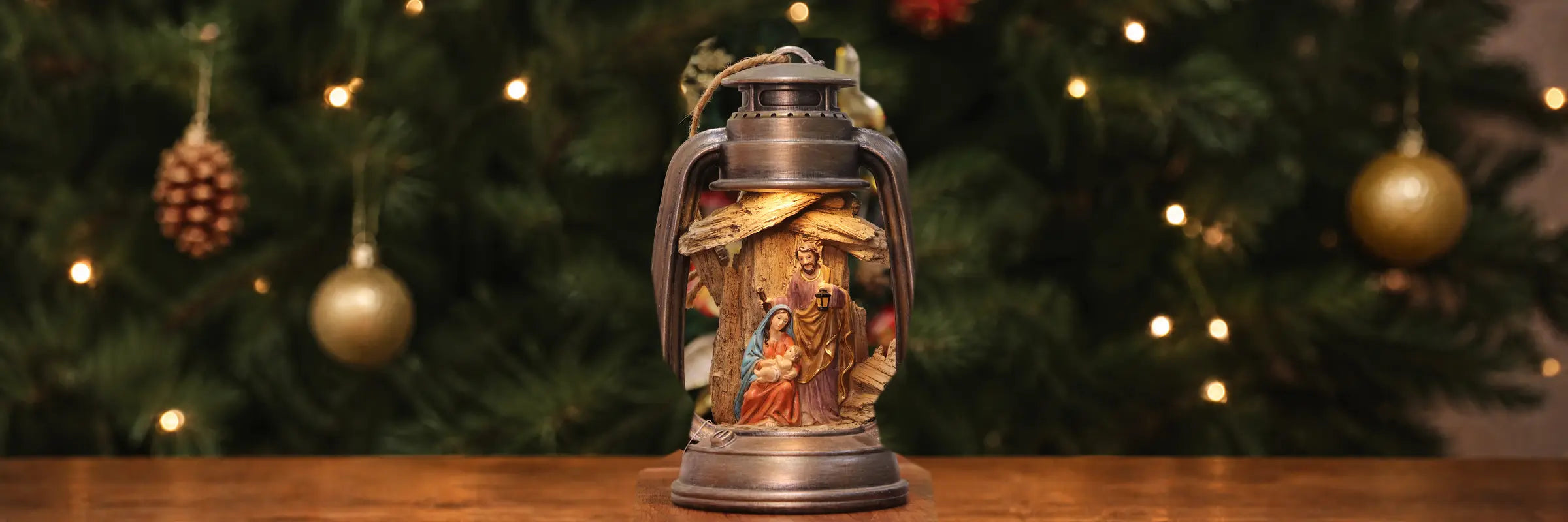 A vintage-style lantern ornament with a hand-painted nativity scene inside, displayed on a wooden surface.