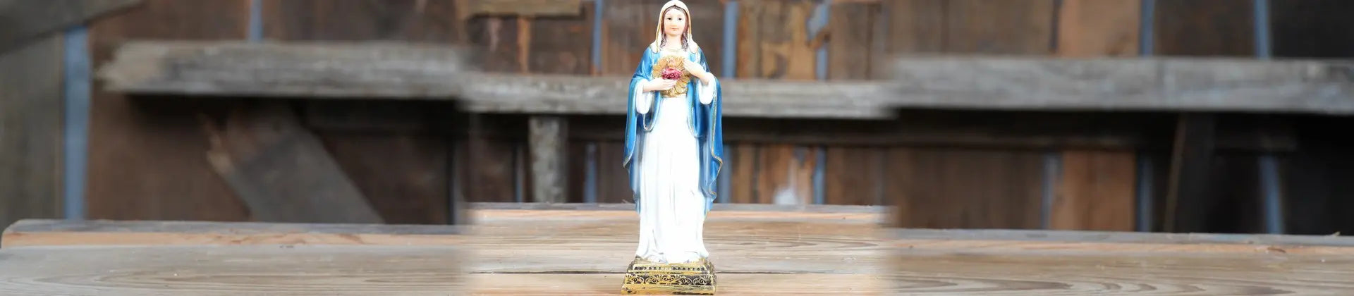 A religious figurine of the Virgin Mary standing on a wooden surface, with a rustic wooden background.
