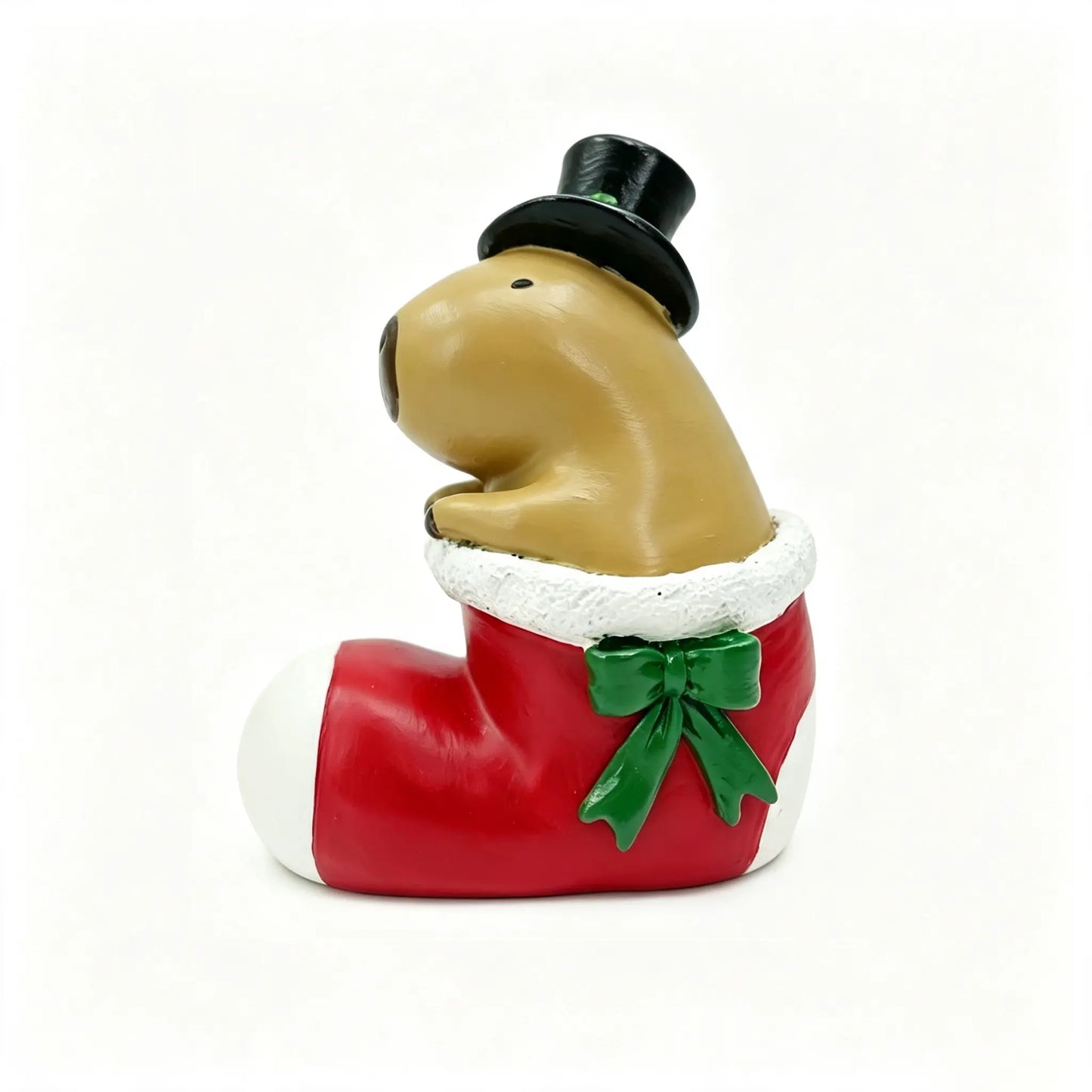 A capybara figurine wearing a black top hat and sitting inside a red Christmas stocking with white trim and a green bow on a white background.