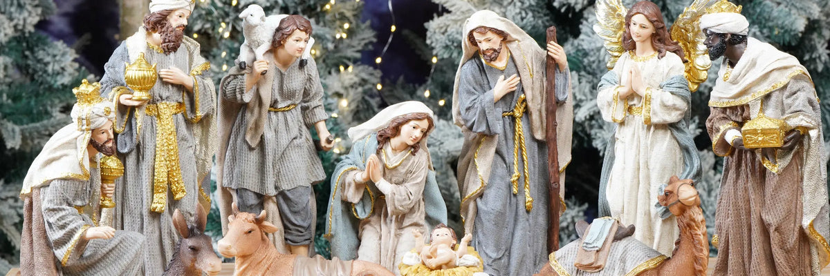 A nativity scene figurine set featuring Mary, Joseph, baby Jesus, wise men, shepherds, and animals, styled with a rustic wooden background and warm string lights.